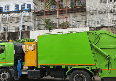 Green garbage truck parked near building